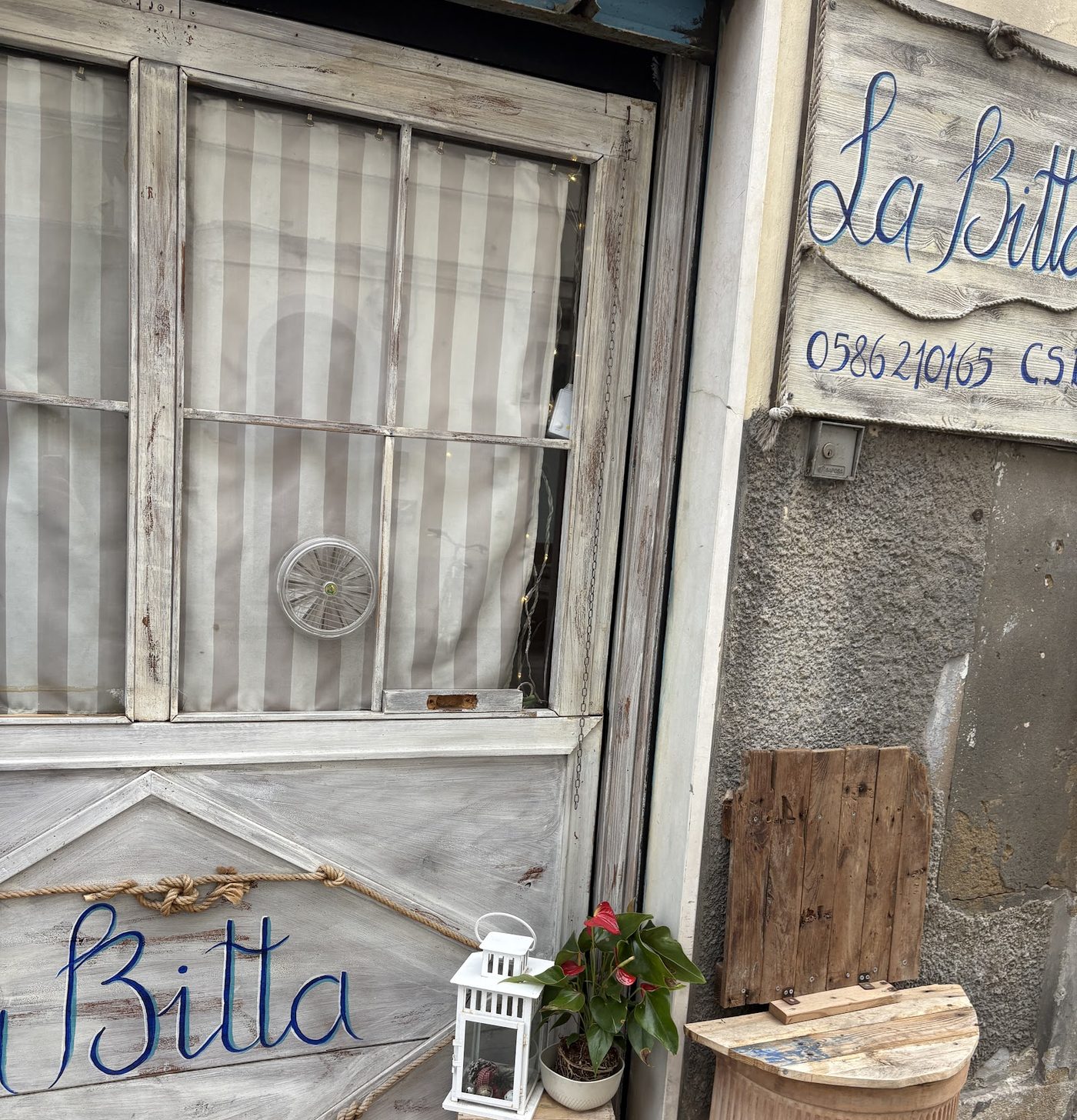 La facciata de La Bitta: porta in legno sbiancato con il nome dipinto a mano in blu, tenda a righe e una lanterna accanto all'ingresso.