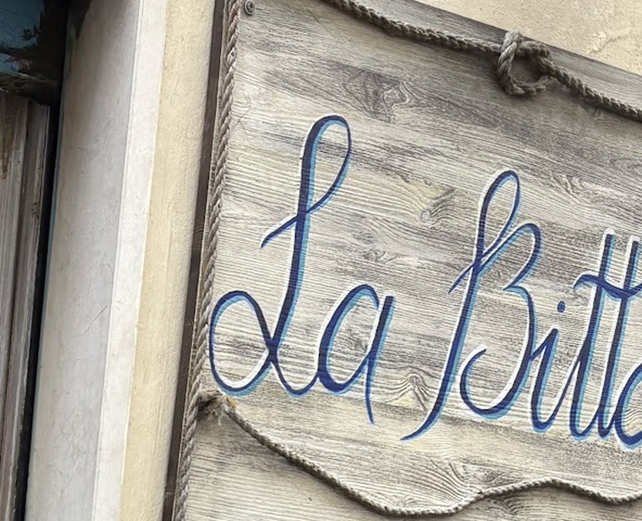 L'insegna in legno de La Bitta, con il nome dipinto a mano in blu e la cornice di corda.