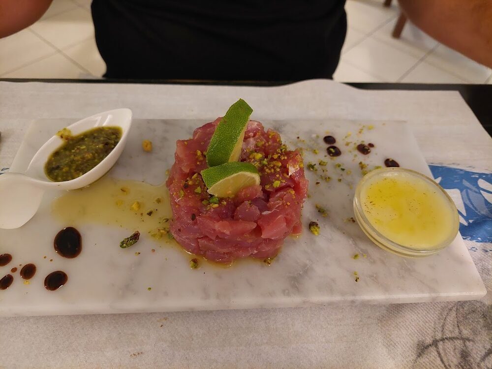 Tartare di tonno su un tagliere di marmo, con granella di pistacchio, lime e due salsine.