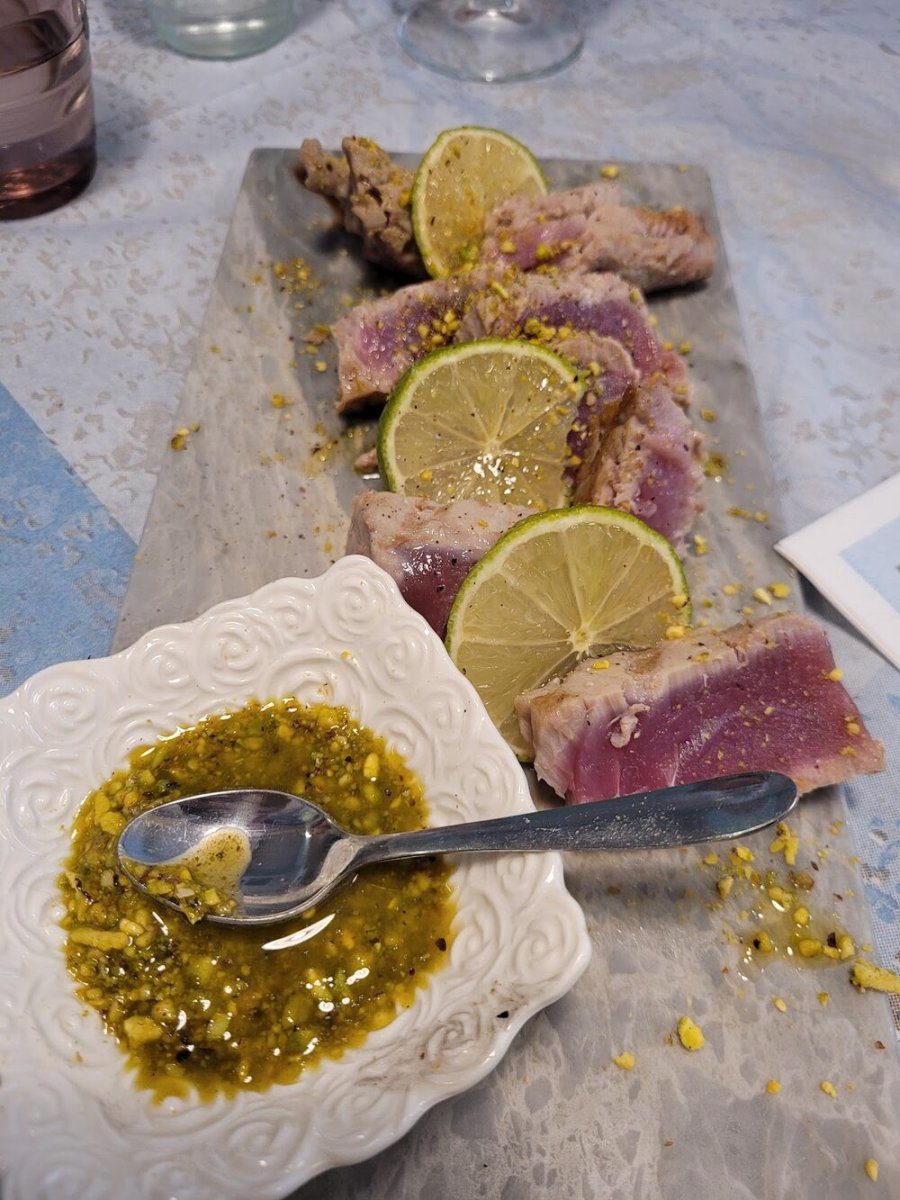 Fette di tonno scottato disposte su un tagliere con lime e granella di pistacchio.
